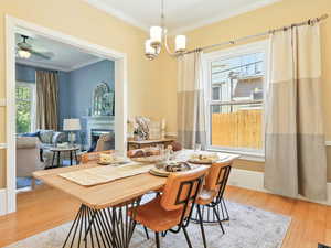 Dining room featuring crown molding, wood finished floors, a fireplace, a chandelier, and ceiling fan
