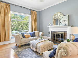 Living area with a fireplace with flush hearth, ornamental molding, and wood finished floors
