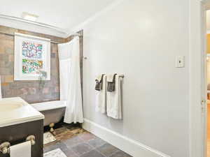Full bathroom featuring stone finish floors, vanity, crown molding, and shower / bath combo