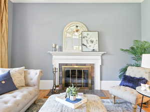 Living area with a fireplace, ornamental molding, and wood finished floors