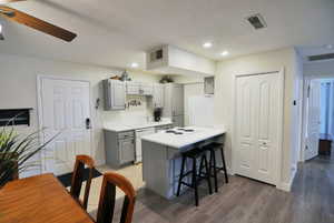 Kitchen featuring gray cabinetry, light countertops, a peninsula, white appliances, and a kitchen bar