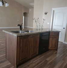 Kitchen featuring dark wood-style flooring, dishwasher, light stone countertops, and a center island with sink
