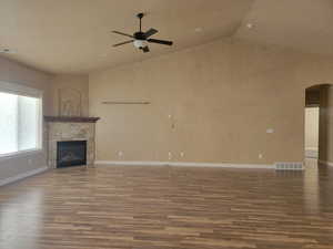 Spacious great room with gas log fireplace, vaulted ceiling, wood finished floors, arched walkways, and ceiling fan
