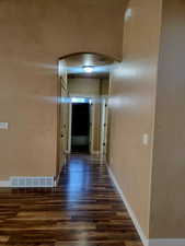 Hall featuring arched walkways, dark wood-type flooring, and a textured wall