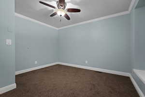 Spare room featuring dark carpet, ornamental molding, a textured ceiling, and a ceiling fan