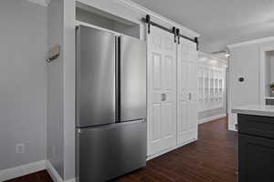Kitchen with freestanding refrigerator, wood finish floors, crown molding, a textured ceiling, and a barn door
