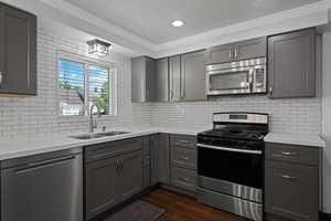 Kitchen with gray cabinets, appliances with stainless steel finishes, wood tiled floors, light stone counters, and crown molding