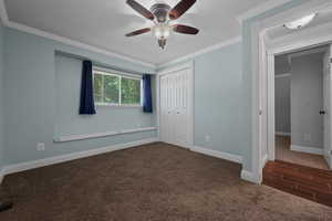 Unfurnished bedroom featuring dark carpet, crown molding, a ceiling fan, and a closet