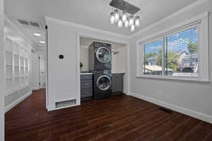 Laundry area with ornamental molding, dark wood finished floors, cabinet space, and estacked washer and dryer