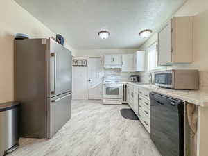 Kitchen with appliances with stainless steel finishes, light countertops, a textured ceiling, tasteful backsplash, and light marble finish flooring