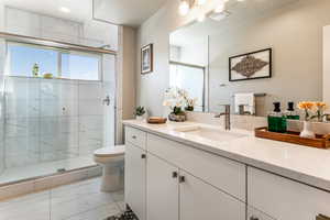 Full bath with marble look tile flooring, vanity, and a marble finish shower