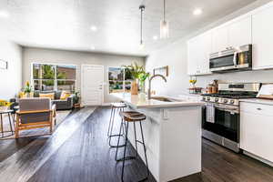 Kitchen featuring appliances with stainless steel finishes, dark wood-type flooring, a kitchen breakfast bar, an island with sink, and recessed lighting
