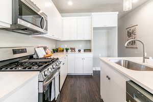Kitchen with stainless steel appliances, dark wood-style flooring, white cabinetry, and light stone counters