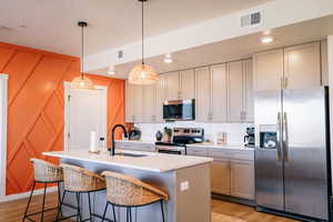 Kitchen with stainless steel appliances, light wood-style flooring, a textured ceiling, light countertops, and an island with sink