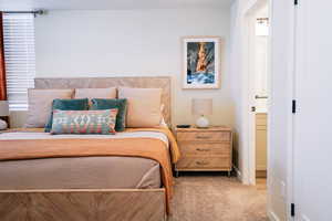 Bedroom with ensuite bathroom and light colored carpet