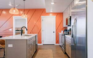 Kitchen with gray cabinetry, appliances with stainless steel finishes, a textured ceiling, light countertops, and a center island with sink