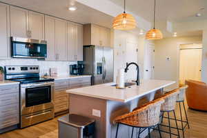Kitchen featuring stainless steel appliances, light wood-type flooring, light countertops, a breakfast bar, and a textured ceiling
