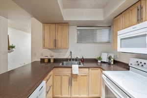 Kitchen with white appliances, dark countertops, light brown cabinets, and a tray ceiling