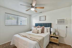 Bedroom with carpet floors, a ceiling fan, and a wall mounted air conditioner