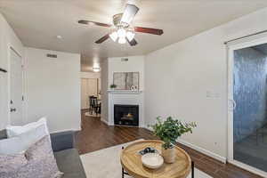 Living area with wood tiled floors, a lit fireplace, and a ceiling fan