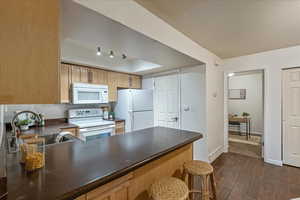 Kitchen with white appliances, dark wood-tiled floors, dark countertops, a peninsula, and a kitchen breakfast bar
