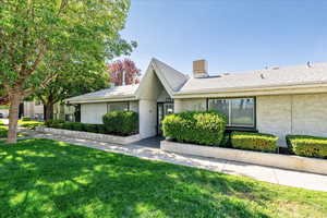 View of front of property with a chimney, a front yard, stucco siding, and roof with shingles