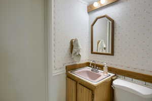 Half bath featuring wallpapered walls, vanity, and wainscoting