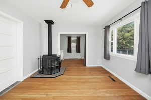 Unfurnished living room with a wood stove, light wood finished floors, and a ceiling fan