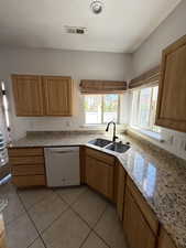 Kitchen with white dishwasher, light tile patterned floors, a textured ceiling, and light stone counters