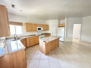 Kitchen with a center island, white appliances, light tile patterned floors, light stone countertops, and recessed lighting