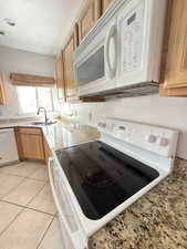 Kitchen with white appliances, light tile patterned flooring, light stone countertops, and light brown cabinetry