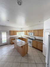 Kitchen with white appliances, light tile patterned floors, a center island, a textured ceiling, and recessed lighting