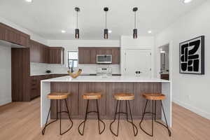 Kitchen with modern cabinets, light countertops, decorative light fixtures, light wood-style flooring, and appliances with stainless steel finishes