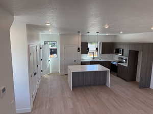 Kitchen featuring modern cabinets, appliances with stainless steel finishes, a kitchen island, a textured ceiling, and light countertops