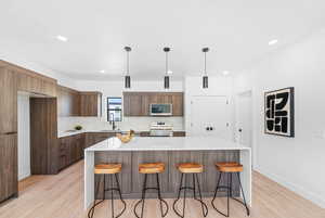 Kitchen with modern cabinets, light wood-style flooring, light countertops, a breakfast bar, and recessed lighting
