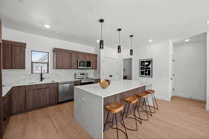 Kitchen with a kitchen island, appliances with stainless steel finishes, tasteful backsplash, a kitchen bar, and light wood-style floors
