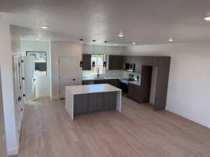 Kitchen featuring stainless steel appliances, a center island, a textured ceiling, light countertops, and light wood finished floors