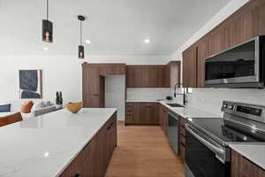 Kitchen with appliances with stainless steel finishes, light wood-type flooring, modern cabinets, pendant lighting, and backsplash