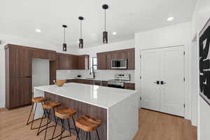 Kitchen featuring modern cabinets, backsplash, stainless steel appliances, a kitchen breakfast bar, and light wood-style floors