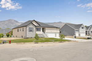 View of front of house with stone siding, a garage, concrete driveway, a mountain view, and a front lawn
