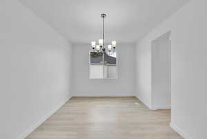 Empty room with light wood-style floors and a chandelier
