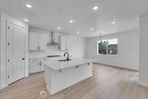 Kitchen with tasteful backsplash, an island with sink, light countertops, light wood finished floors, and recessed lighting