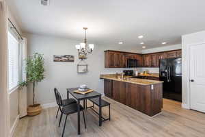 Kitchen featuring black appliances, a peninsula, dark brown cabinetry, a chandelier, and light wood-style floors