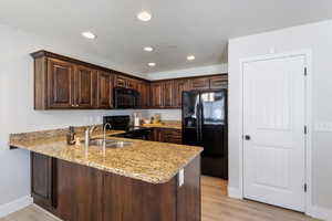 Kitchen with black appliances, a peninsula, light stone counters, dark brown cabinets, and recessed lighting