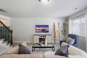 Living room with a glass covered fireplace, wood finished floors, and stairway