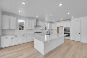Kitchen featuring white cabinetry, double oven, light countertops, a center island with sink, and recessed lighting