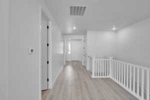 Hallway featuring an upstairs landing, light wood finished floors, and recessed lighting