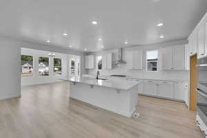 Kitchen with decorative backsplash, a chandelier, double oven, a center island with sink, and white cabinetry