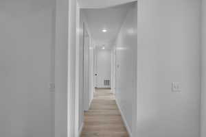 Corridor with light wood-type flooring and recessed lighting