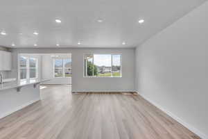 Unfurnished living room with light wood-type flooring, a chandelier, a textured ceiling, and recessed lighting